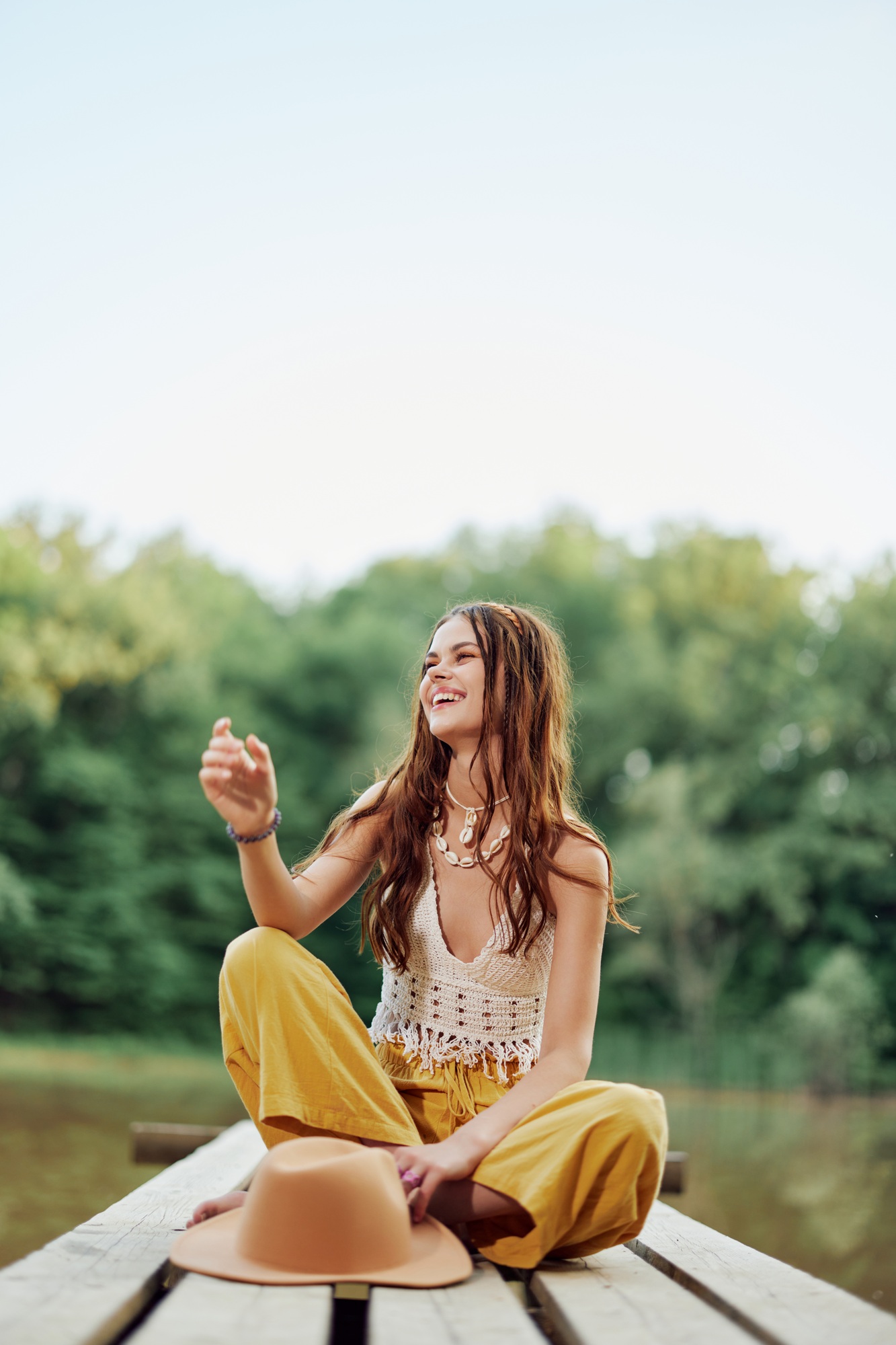 A hippie woman sits on a bridge by a lake on a nature trip and smiles in eco-clothing. The concept