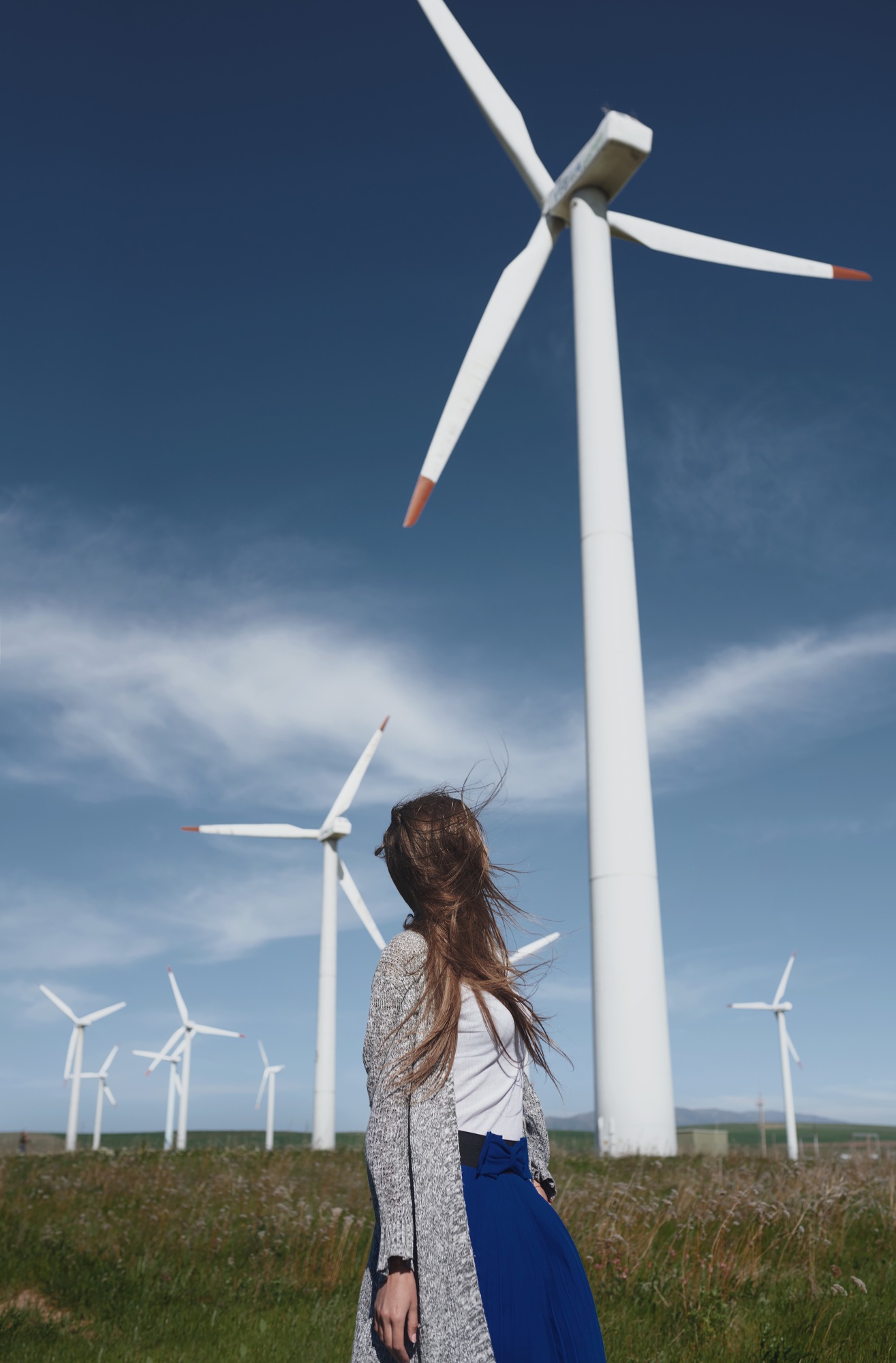 Woman with long tousled hair next to the wind turbine with the wind blowing